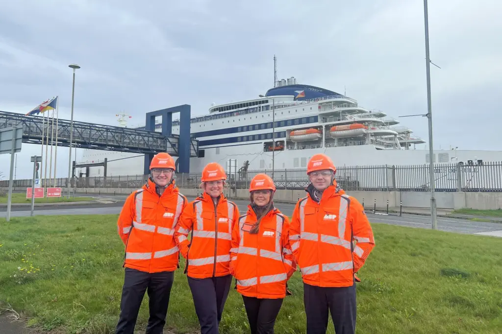 A group of people in orange jackets and helmets standing in front of a large ship in Hull