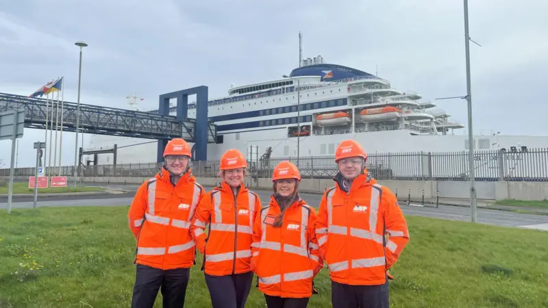 A group of people in orange jackets and helmets standing in front of a large ship in Hull