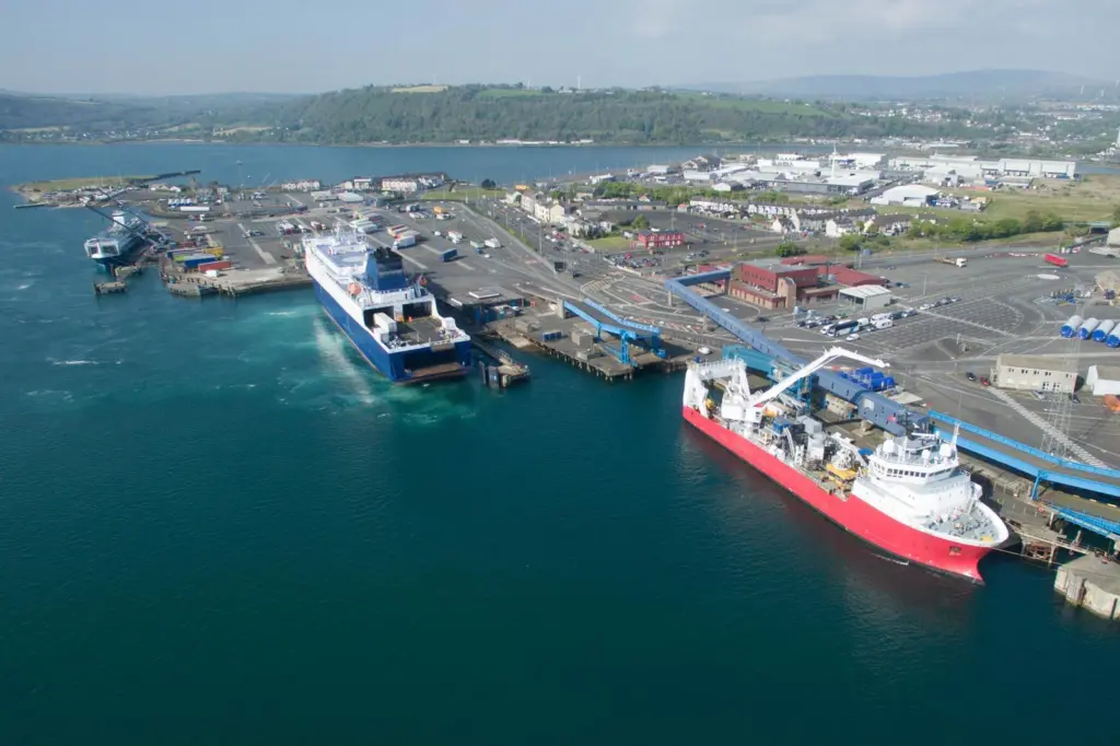 The image shows a wide angle shot of Larne Harbour with a ferry and workboat in the foreground