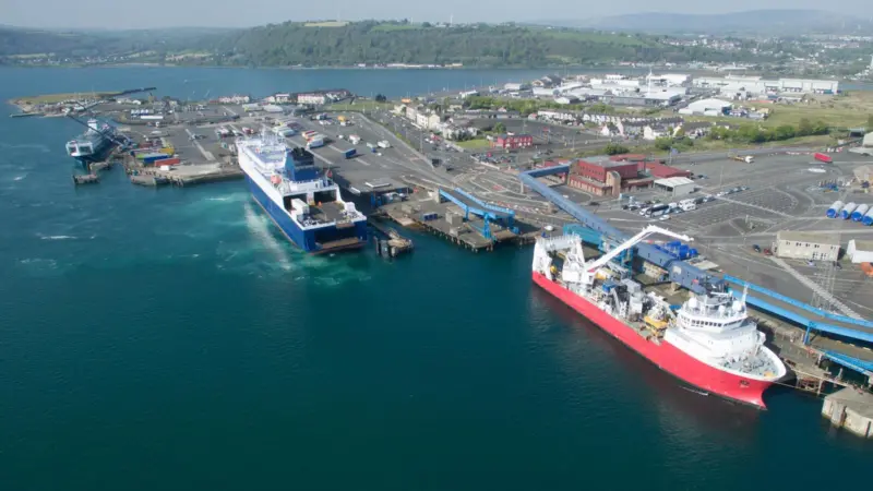 The image shows a wide angle shot of Larne Harbour with a ferry and workboat in the foreground