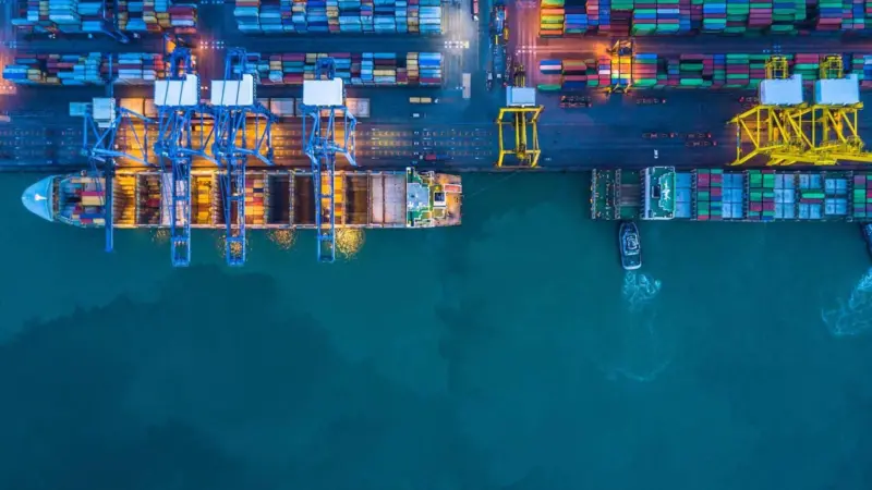 The image shows vessels berthed at a terminal with a container yard in the background