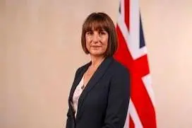 The image shows Rachel Reeves dressed in a grey suit standing in front of the Union Jack flag