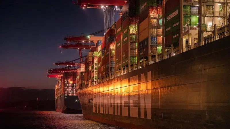 The image shows a ship berthed at a lit up dock at night