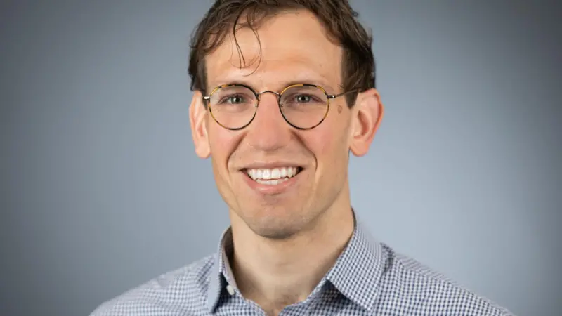A picture of Cameron Gook, a white man wearing glasses and a blue shirt