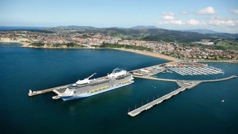 A cruise ship docks at the Port of Bilbao, Spain with mountains in the background