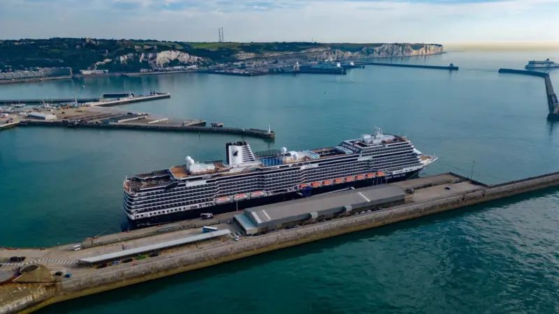 The pictures shows a Holland America Line cruise ship against a backdrop of the White Cliffs of Dover