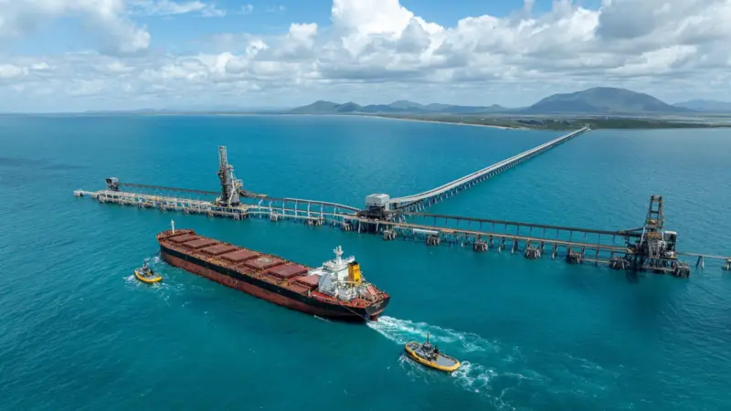 A ship with two tugs at the end of a very long pier at NQXT Port