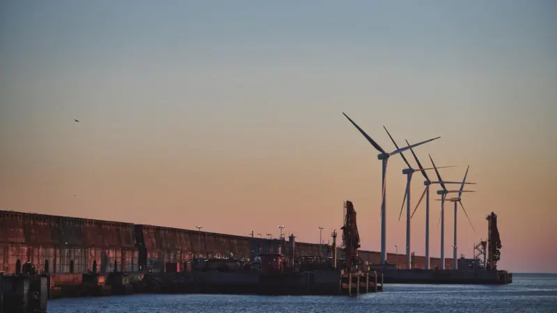 The image shows Bilbao Port by sunset with wind turbines in the background