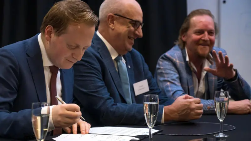 The image shows Photo: Mark Lengton, Joseph Krapf and Paul Vosbeek signing the agreement