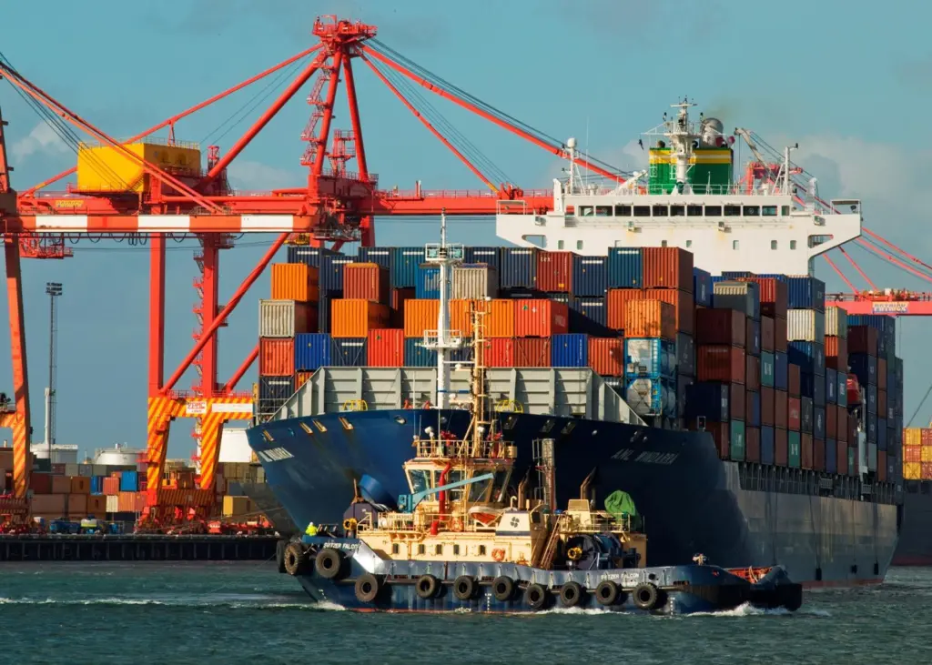 A large container ship being pulled into port by a tugboat