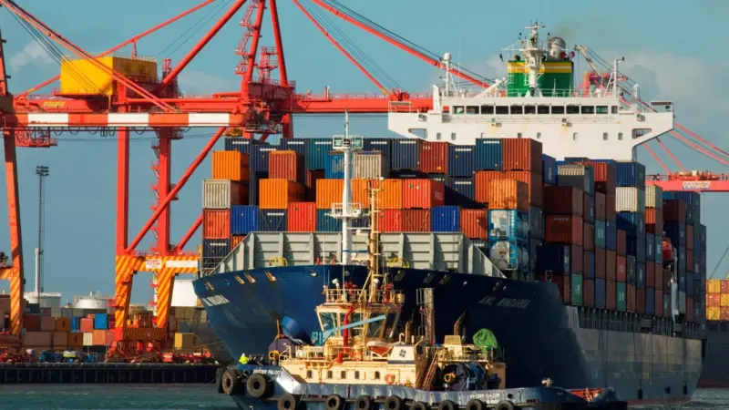 A large container ship being pulled into port by a tugboat