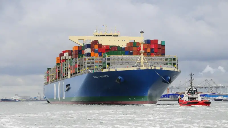 A bulk cargo carrier being pulled by a tugboat.