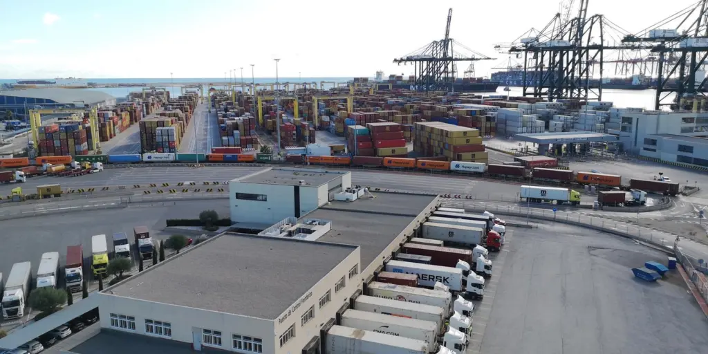 Port of Valencia showing a warehouse in the foreground with trucks and containers and cranes in the background