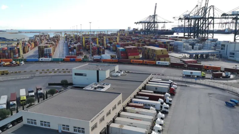 Port of Valencia showing a warehouse in the foreground with trucks and containers and cranes in the background