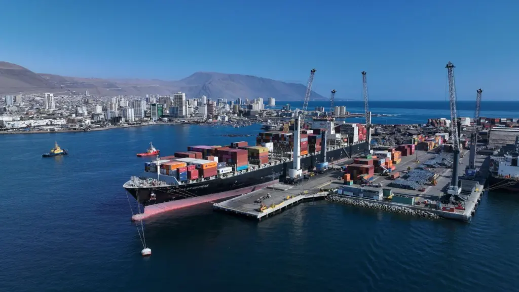 Iquique Terminal Internacional in Chile. Image shows a container ship at port with the city and low mountains behind