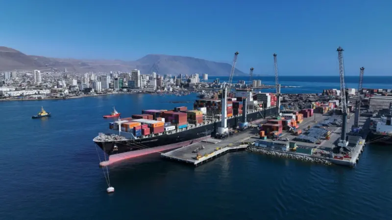 Iquique Terminal Internacional in Chile. Image shows a container ship at port with the city and low mountains behind