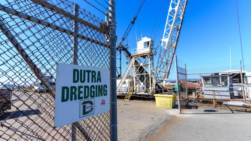 A Dutra dredging sign on a fence with a crane behind