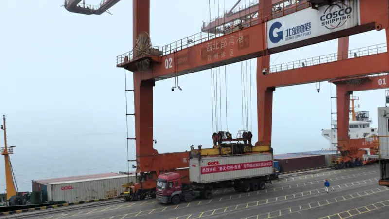 An OOCL truck sits beneath a large crane as its container is loaded