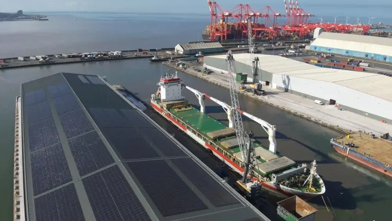 Port of Liverpool showing a warehouse to the left with solar panels on the roof, a ship at dock, warehouses to the right and cranes in the background