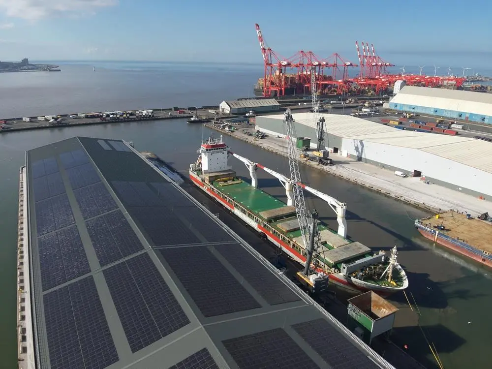 Port of Liverpool showing a warehouse to the left with solar panels on the roof, a ship at dock, warehouses to the right and cranes in the background