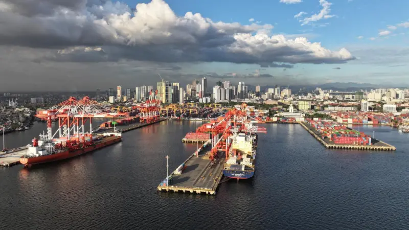 Manila South Harbour, Philippines, showing ships portside, a number of ship-to-shore cranes and high rise buildings in the background