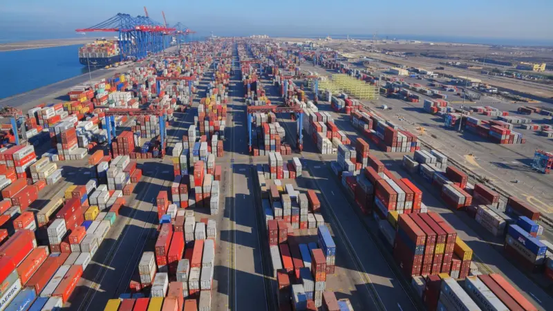 Containers at the Suez Canal Container Terminal with a shit and cranes to the left background