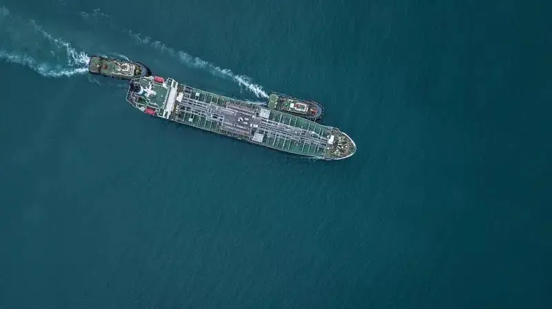 An aerial shot of a cargo ship at sea with two tugs