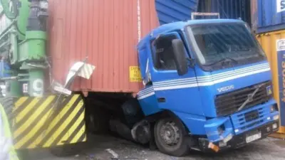 A blue Volvo lorry squashed underneath collapsed shipping containers