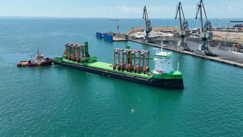 Eight hybrid straddle carriers arrive on a green barge at the Port of Thessaloniki